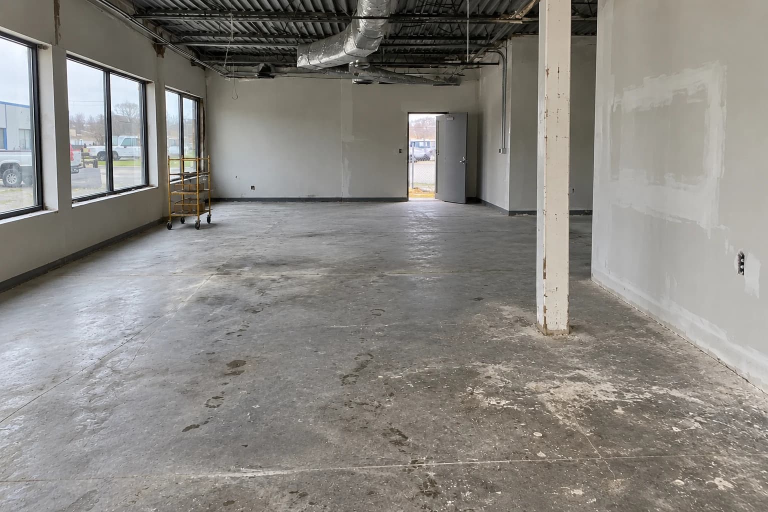 Generated after example: the same commercial unit from a separate camera view, with loose waste removed and worn concrete and unfinished walls unchanged