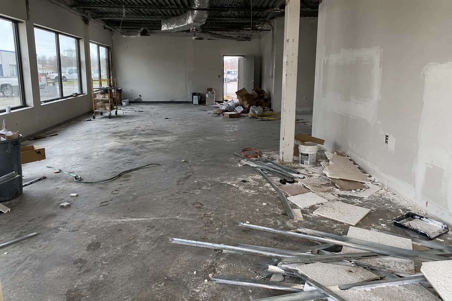 Generated before example: an older commercial unit with ceiling-tile waste, metal offcuts, packaging and dust beside patched walls