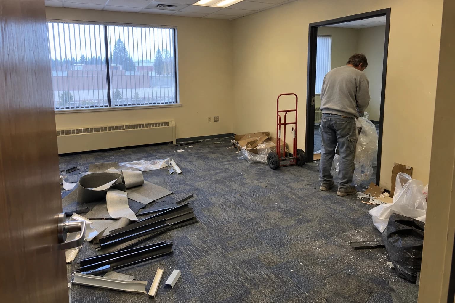 Generated during cleanup example: a worn office suite with carpet offcuts, door trim, packing waste and a worker collecting wrapping